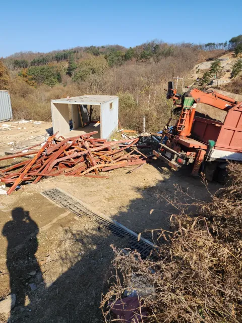 철거된 주황색 철골 고철 더미와 운반 트럭이 있는 현장